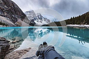 Legs of traveler relaxing on Moraine Lake with rocky mountains in gloomy day at Banff national park