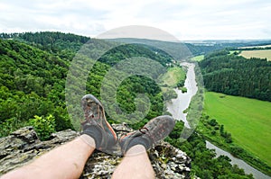 Legs of traveler sitting on a high mountain top and looking on river landscape. Natural freedom concept