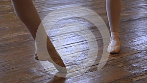Legs of two girls in ballet shoes doing demi plie during ballet class in frayed ballet classroom.