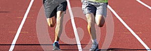 Legs of two runners running together on a track in sunshine