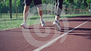 Legs of unrecognizable fit man and woman running on sunny track outdoors. Sportive Caucasian couple in sneakers jogging