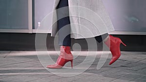 Legs of unrecognizable woman in red boots walking in autumn street