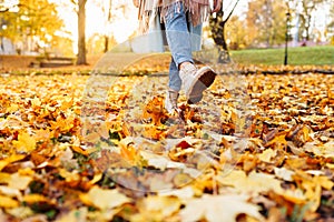 Legs of unrecognosable woman wearing brown boots and jeans in autumn yellow foliage walking in park or forest