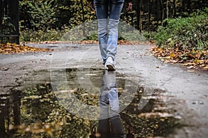 Legs in white sneakers reflected in a puddle. Reflection of girl wearing white shoes in water puddle