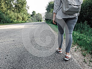 Legs of a woman with a backpack walking along a rural road