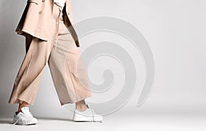 Legs of woman in beige business smart casual suit and sneakers walking over light. Stylish business female wear