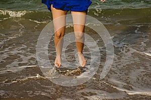 Legs of woman in blue dress jumping on the shore of the beach