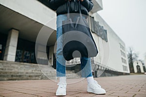 Legs of a woman holding a black eco bag on the background of the building
