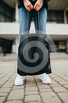 Legs of a woman holding a black eco bag on the background of the building