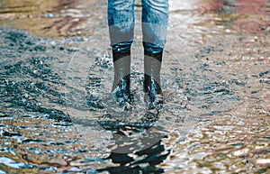 Legs of woman in shabby jeans with black rubber boots standing in a puddle of water after rain