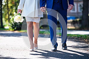 Legs of a woman in a white dress and a man in a blue suit walking in the park