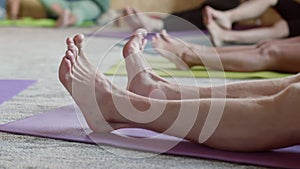Legs of women sitting on mat doing warming exercises during yoga practice.