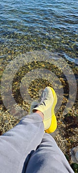 Legs in yellow sneakers are hung on water, on a trip by nature, tourism, sea and sneakers