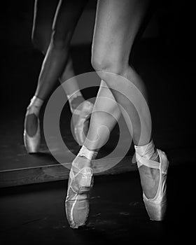 Legs of young ballerina with pointe shoes dancing on a black floor background. Ballet practice.