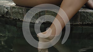 Legs of a young and beautiful European girl in a swimming suit close-up sitting near swimming pool with barefoot wet legs