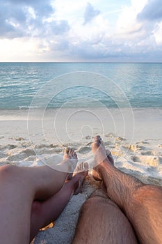 The legs of a young couple in love, who sit on the beach and see off the sunset