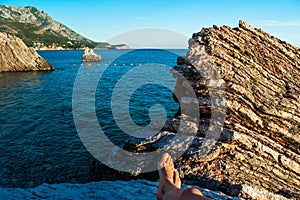 Legs of young girl on beautiful rocks on pebble public stone beach. Rafailovici esort towns. Mountenegro. Adriatic Sea