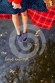 Legs of a young girl near the lake on a plaid in a red cage. Beautiful reflection in the water. View from above. The inscription