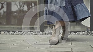 The legs of a young girl in a spring blue dress walk along the road