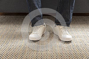 Legs of a young male fashion white sneakers stand on carpet in a room.