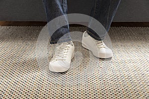 Legs of a young male fashion white sneakers stand on carpet in a room.