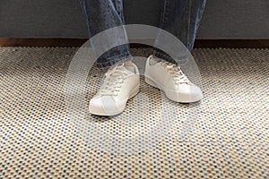 Legs of a young male fashion white sneakers stand on carpet in a room.