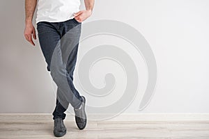 Legs of a young man in jeans and sneakers on gray background