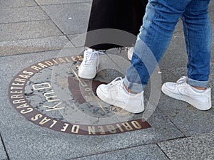 Legs of young people step on zero kilometre sign in Puerta del Sol square in Madrid, Spain