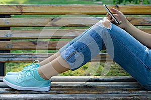 Legs of a young woman in jeans on a bench in the park