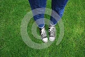 Legs of young woman standing on green grass in park