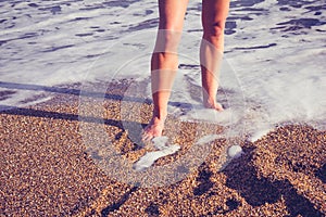 The legs of a young woman walking in the surf on beach