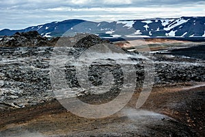 Leirhnjukur old black lava field with colorful stones and smoke coming from ground and blue sky in Iceland, overcast day in summer