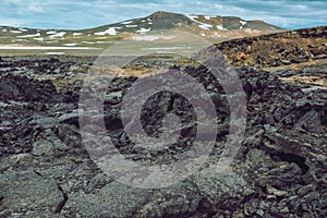 Leirhnjukur old black lava field, green mountains with snow and blue sky in Iceland, overcast day in summer , film effect with