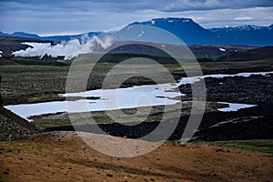 Leirhnjukur old black lava field with snow and colorful stones and smoke coming from ground and blue sky in Iceland, overcast day