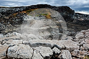 Leirhnjukur old black lava field with stones and smoke coming from ground and blue sky in Iceland, overcast day in summer , film