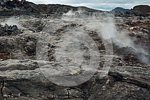 Leirhnjukur old black lava field with stones and smoke coming from ground in Iceland, overcast day in summer , film effect with