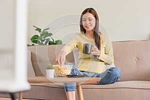 Leisure activity concept, Young woman drinking coffee and eating popcorn while watching television
