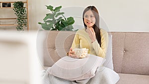 Leisure activity concept, Young woman eating popcorn while sitting on couch to watching television