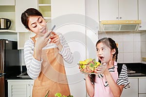 Leisure activity in a kitchen at home. Mom and little girl enjoy takes a photo of vegetable salad