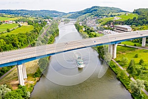 A leisure boat under high bridge where A13 motorway meets 8 highway over Moselle river. Aerial view of Schengen town center.
