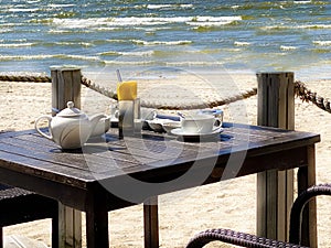 Leisure cafe on beach at sea ,summer holiday restaurant table with cup coffee tea and glass of white wine blue sky sunlight beams