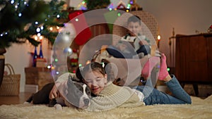 Leisure for children at Christmas. A boy with a book in a rocking chair, a girl near the Christmas tree playing with a