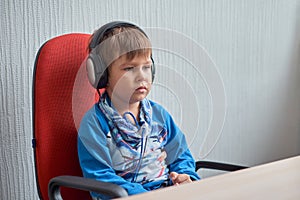 Leisure, education, children, technology and people concept - boy with computer and headphones at office