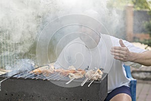 leisure, food, people and holidays concept - happy young man cooking meat on barbecue grill at outdoor summer party