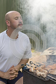 leisure, food, people and holidays concept - happy young man cooking meat on barbecue grill at outdoor summer party. vertical phot