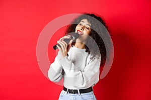 Leisure and hobbies concept. Stylish young woman singing karaoke, looking aside and holding microphone, performing song