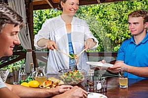 Leisure, holidays, people and food concept - happy friends having lunch and sharing salad at summer garden party