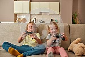 Leisure moments. Excited kids, little boy and girl looking focused while playing video games using joystick or