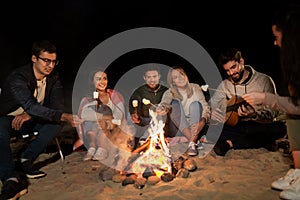 Friends roasting marshmallow on camp fire on beach