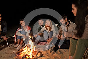 Friends roasting marshmallow on camp fire on beach